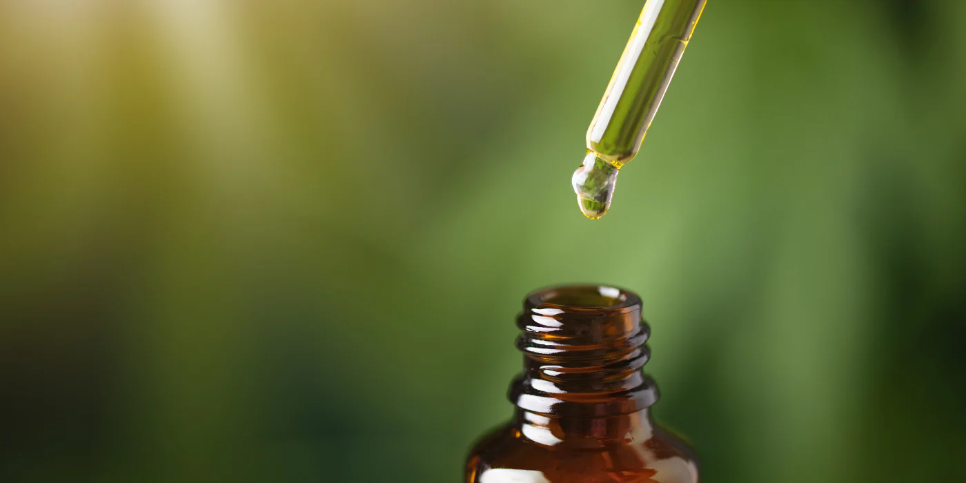 Oil dropper above an open amber glass bottle