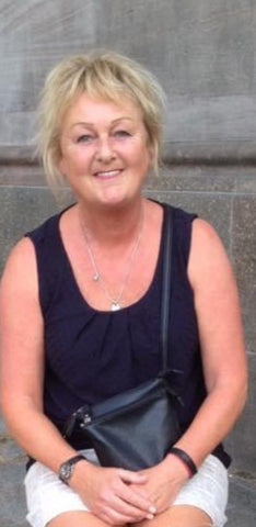 Seated woman in a sleeveless dark top against a grey wall
