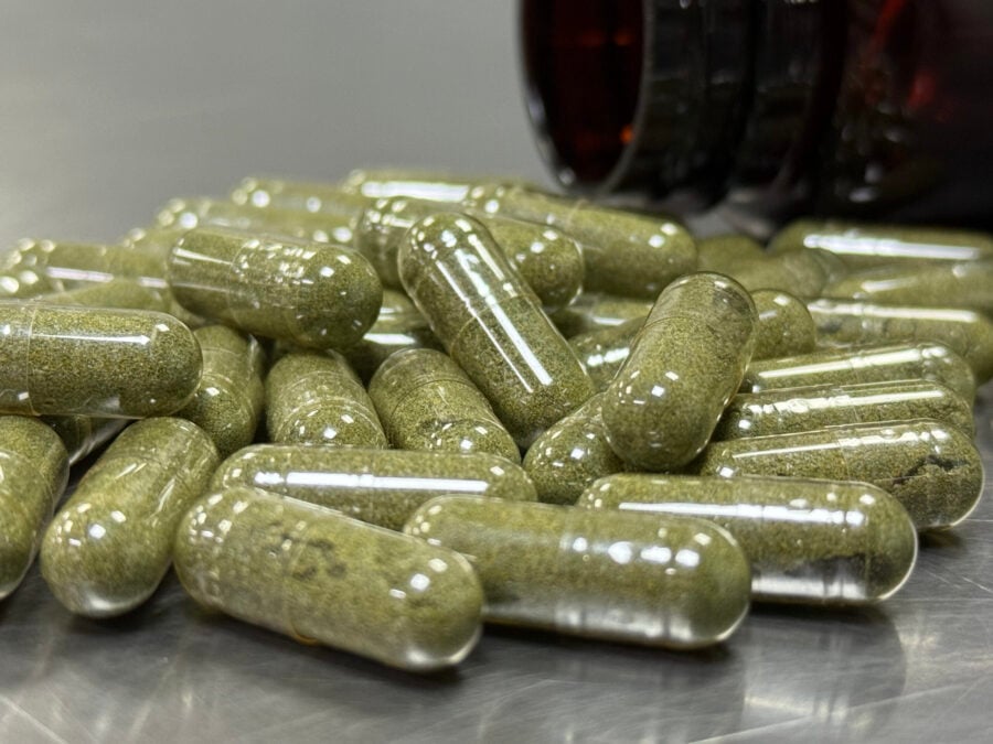 Pile of green capsules in front of a dark bottle
