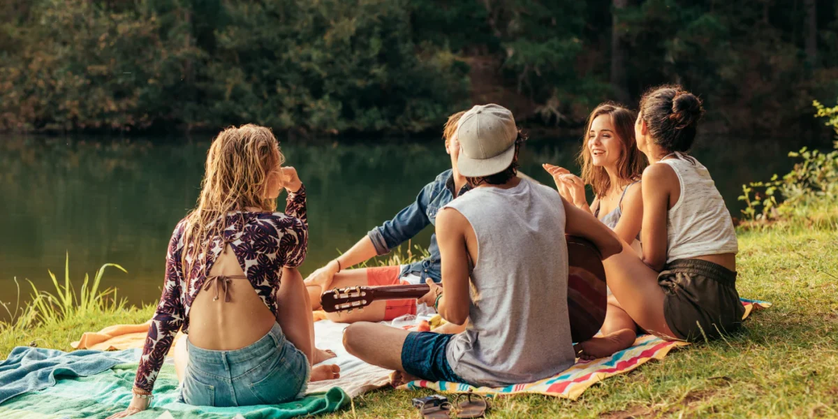 Group of young adults sitting by a lake with a guitar